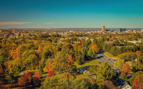 Photo shows an ariel view of autumn trees with a city in the distance. 