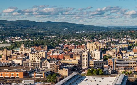 Photo shows wide shot of a city skyline with a mountain landscape in the background. 