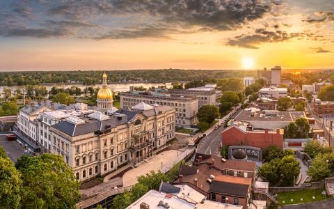 Photo shows aerial view of a city with large historic buildings with one central road and a sunset on the skyline.