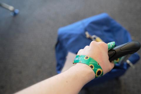 A bag on the floor at an airport gate with a Sunflower Network Lanyard attached to it and the wrist of the person pulling the bag